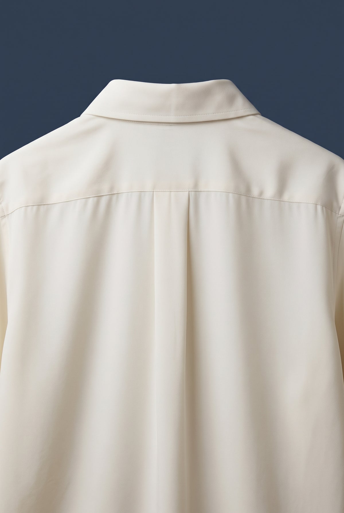 Close-up of the back of a cream-colored long-sleeve button-down shirt, showing the collar, shoulder seam, and fabric texture against a dark navy background.